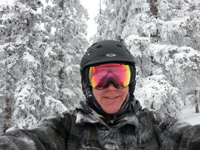 A man wearing a helmet and goggles taking a selfie in the snow.