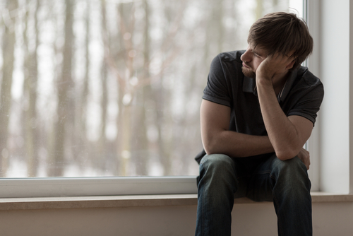 A man sitting on a window sill with his hand on his head.