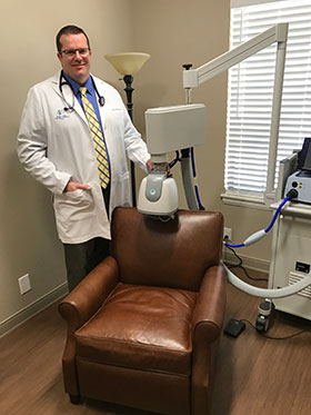 A doctor standing next to a chair and a machine.