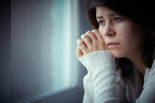 A woman in distress looking at the window wearing white