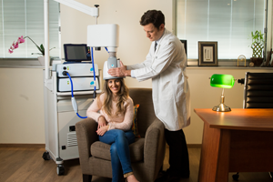 A man in a white coat holding a machine to a woman's head.